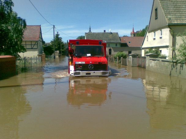 Feuerwehrfahrzeug fährt durch eine überflutete Straße