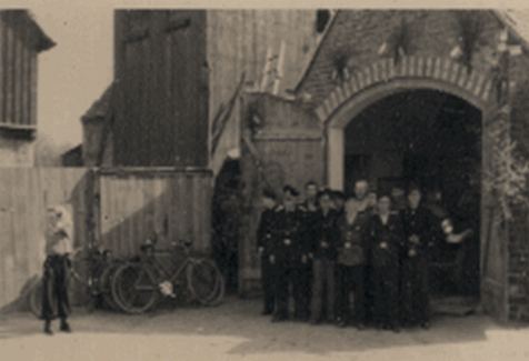 Feuerwehrleute vor dem alten Gerätehaus mit Steigerturm aus Holz