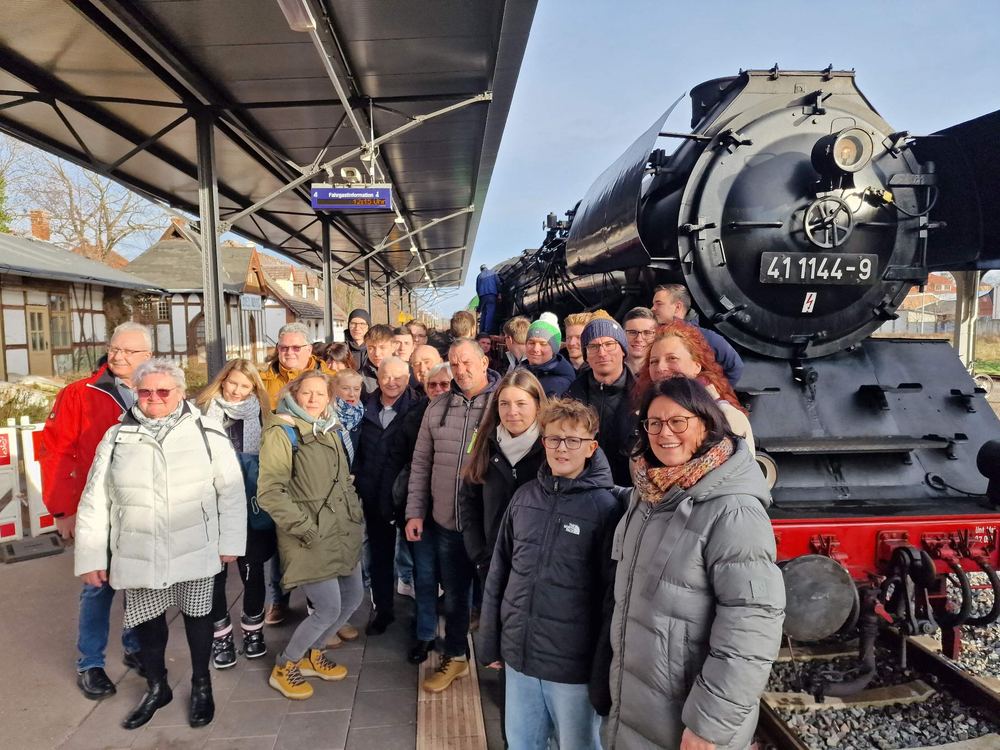 Große Gruppe der Feuerwehr Machern vor einer Dampflokomotive am Bahnsteig