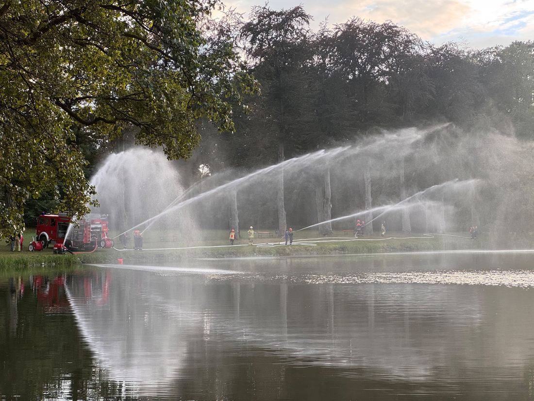 Jugendfeuerwehr Machern bei einer Wasserübung: mehrere Strahlrohre spritzen über einen Teich, links das LF 20