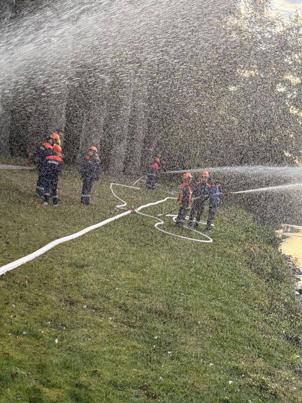 Jugendfeuerwehr mit Schläuchen und Strahlrohren auf einer Wiese im Sprühnebel