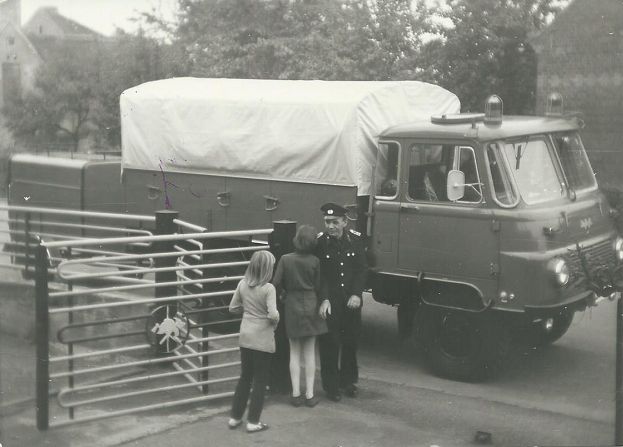 LF 8 auf Robur mit Anhänger, davor ein Feuerwehrmann mit zwei Kindern